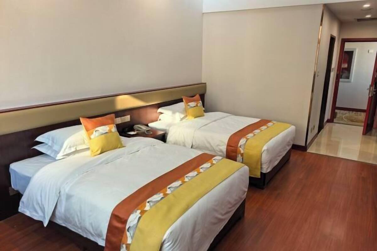 Habitació d'hotel amb dos llits, terres de fusta i una tauleta de nit amb un telèfon.