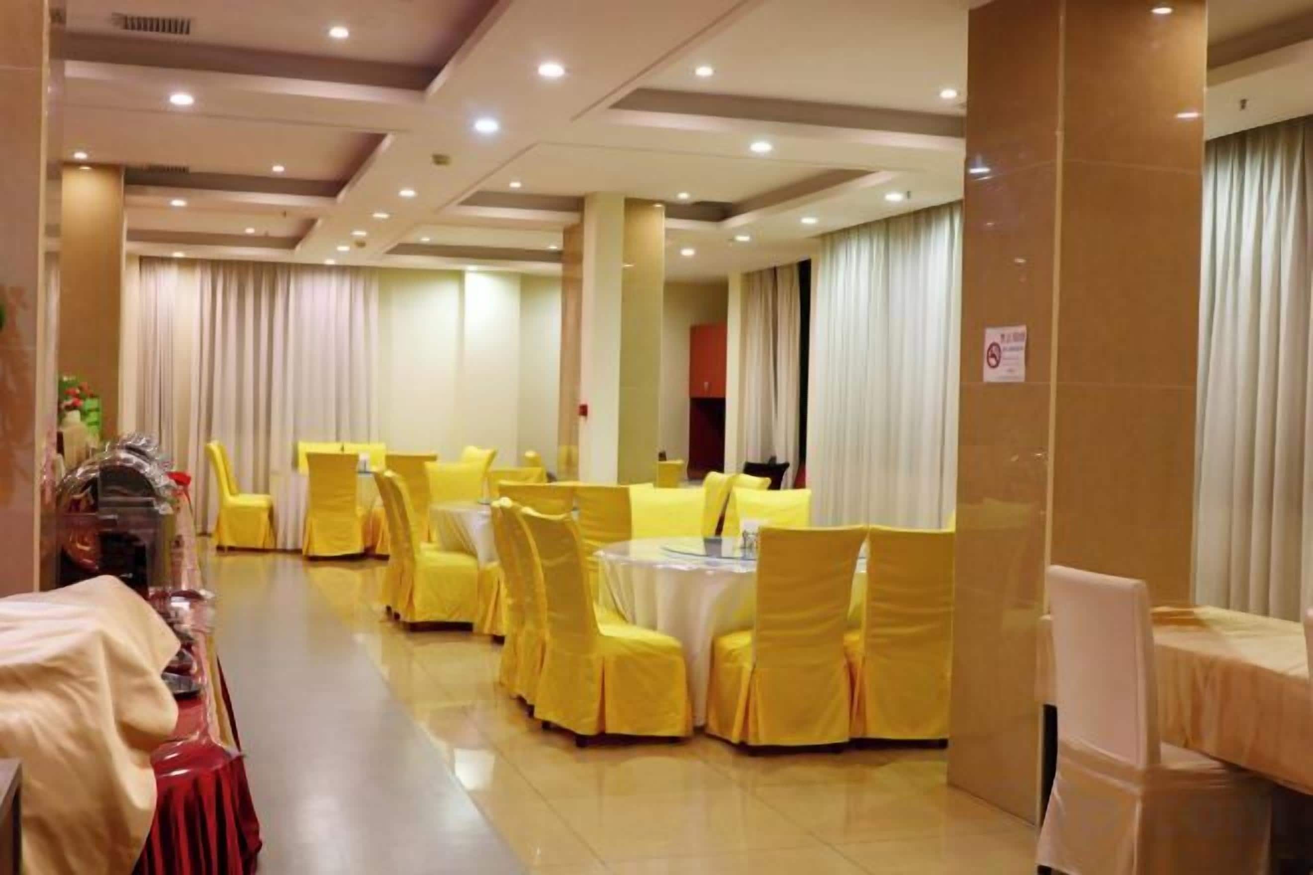 A banquet hall with round tables and chairs, a buffet area, and a large window with curtains.