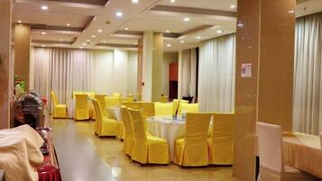 A banquet hall with round tables and chairs, a buffet area, and a large window with curtains.