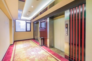 Um corredor com carpete estampado, um elevador e uma lixeira.