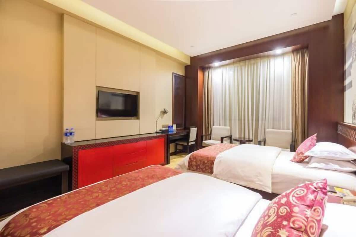 Habitació d'hotel amb dos llits, un escriptori, una cadira, un televisor i una finestra amb cortines.