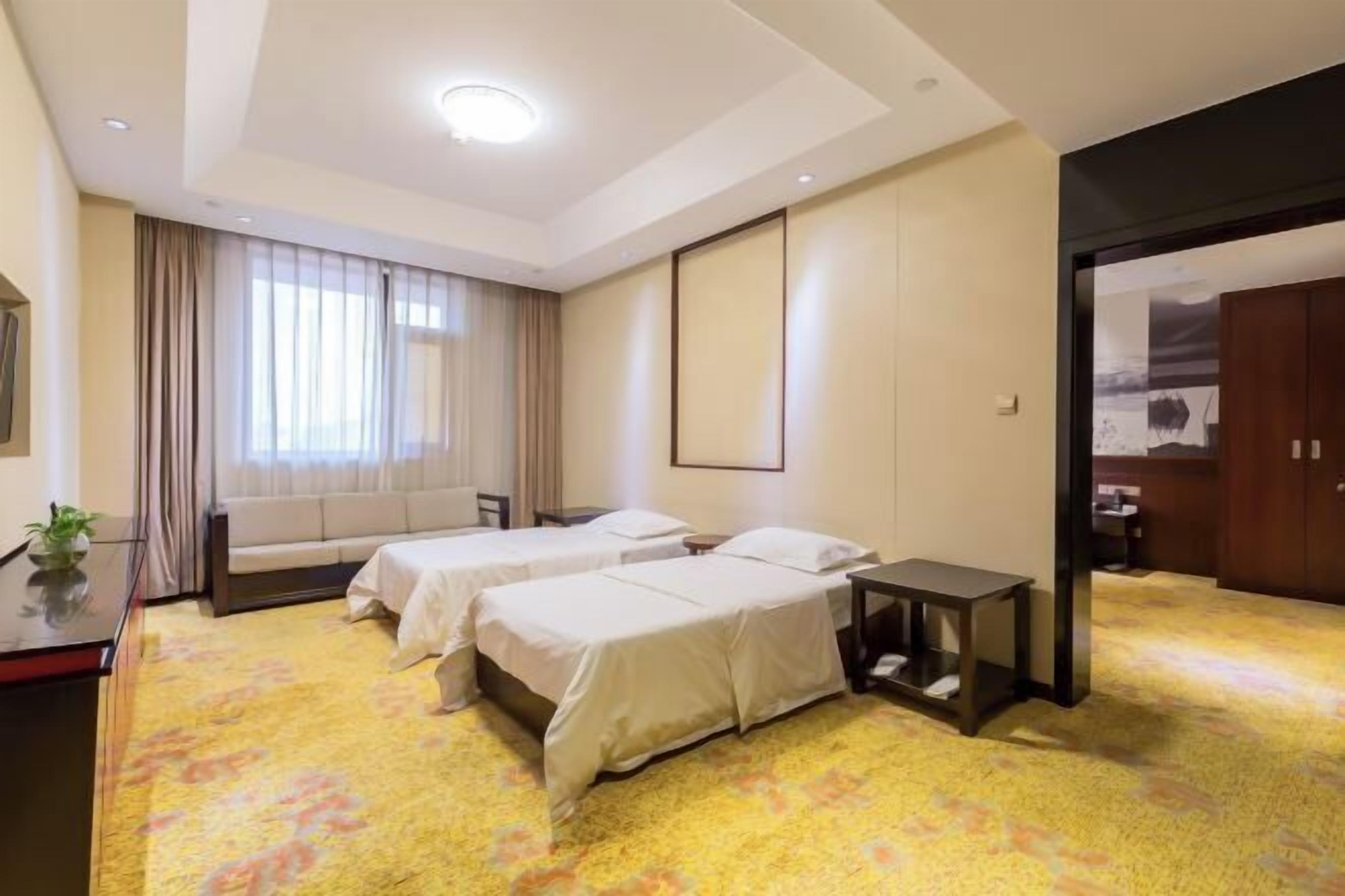 A hotel room with two beds, a sofa, a desk, and a small table.