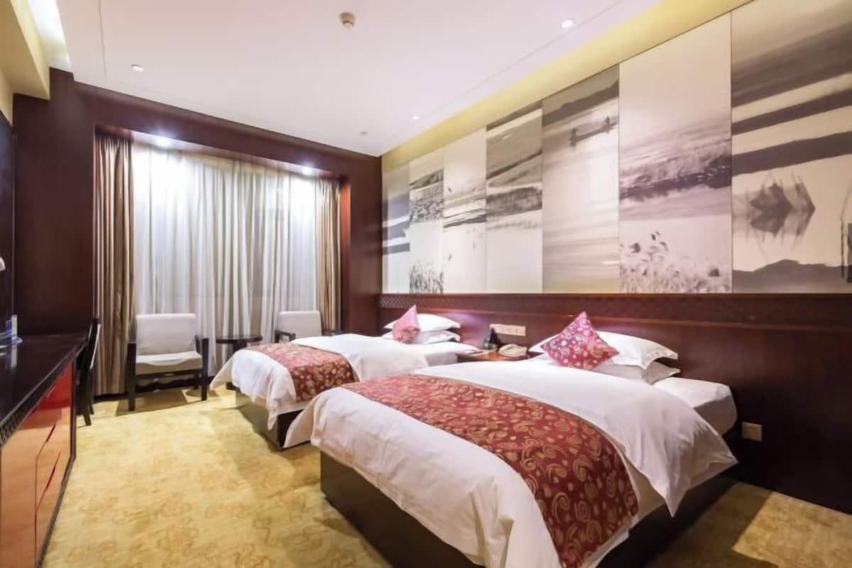 Habitació d'hotel amb dos llits, un escriptori, una cadira i un gran quadre abstracte a la paret.