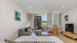 Une chambre d’hôtel moderne équipée d’un lit, d’un canapé, d’une télévision et d’un balcon avec une table et des chaises.
