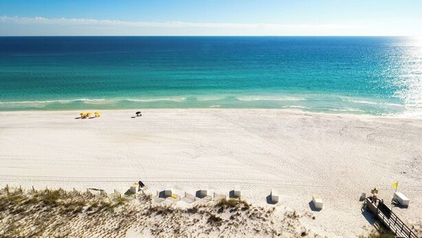 Ein weiter Sandstrand mit klarem, blauem Wasser und einigen Sonnenschirmen.