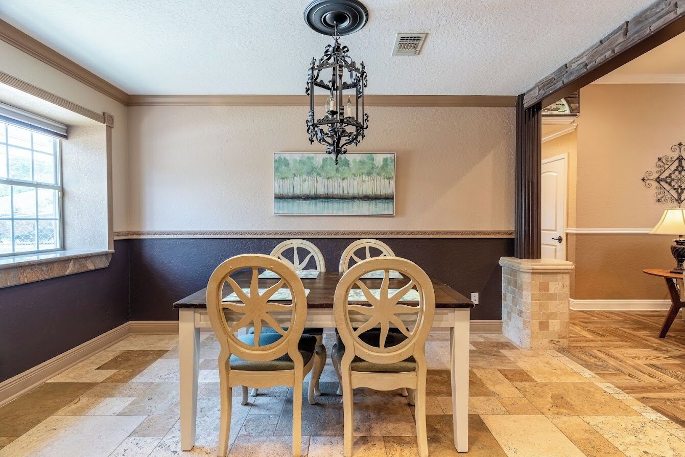 A dining area with a dark wood table and chairs, a chandelier, and a painting on the wall.