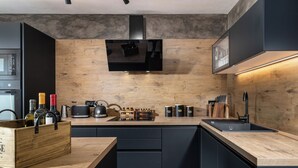 A modern kitchen with a wooden countertop, black cabinets, a built-in microwave, and a range hood.