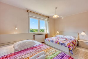 A bedroom with two beds, a window with curtains, a radiator, and a ceiling light.