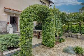 Step into a serene outdoor oasis with a stone pathway leading to a covered seating area, surrounded by lush greenery.