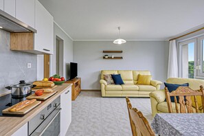 A modern kitchen with a stove, oven, and a wooden countertop. There is a dining area with a table and chairs, and a sofa in the living room.
