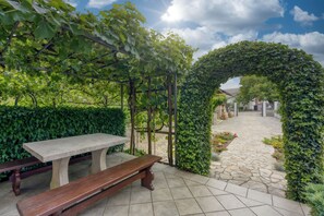 Relax in the serene outdoor patio area with a stone-tiled floor and a comfortable bench beneath a lush pergola.