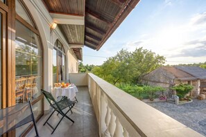 A balcony with a table set for breakfast, overlooking a garden and a stone building. - Teran Karst Apartment with Balcony, Sežana, Slovenia (Sežana)