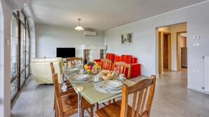 A dining area with a table set for four, a sofa, and a television in the background.