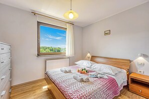 Ein Schlafzimmer mit einem hölzernen Bett, einem Fenster mit Ausblick, einem Nachttisch und einem Beistelltisch.