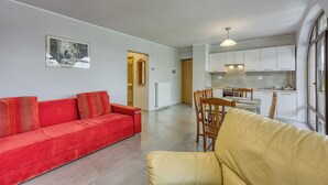 A modern apartment with a red sofa, yellow armchair, and a dining area with wooden chairs and a table.