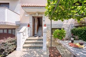 A hotel entrance with a stone facade, a staircase leading to the entrance, and a terrace with a table set for dining and a wine bottle.