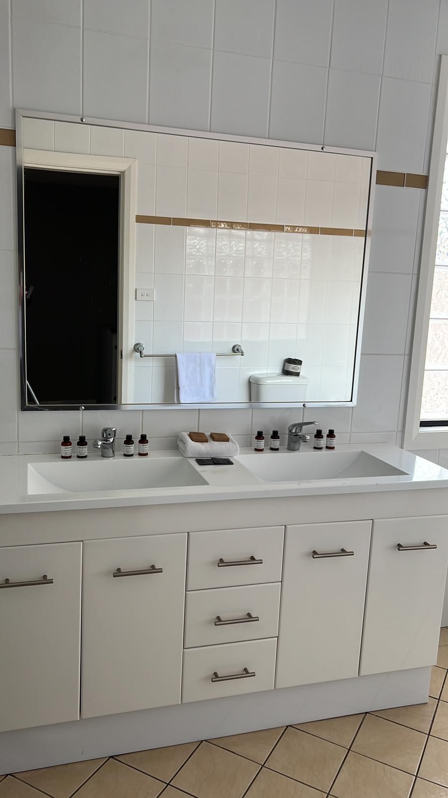 A modern bathroom with two sinks, a large mirror, and a toilet. There are storage cabinets below the sinks and a towel rack above the toilet.