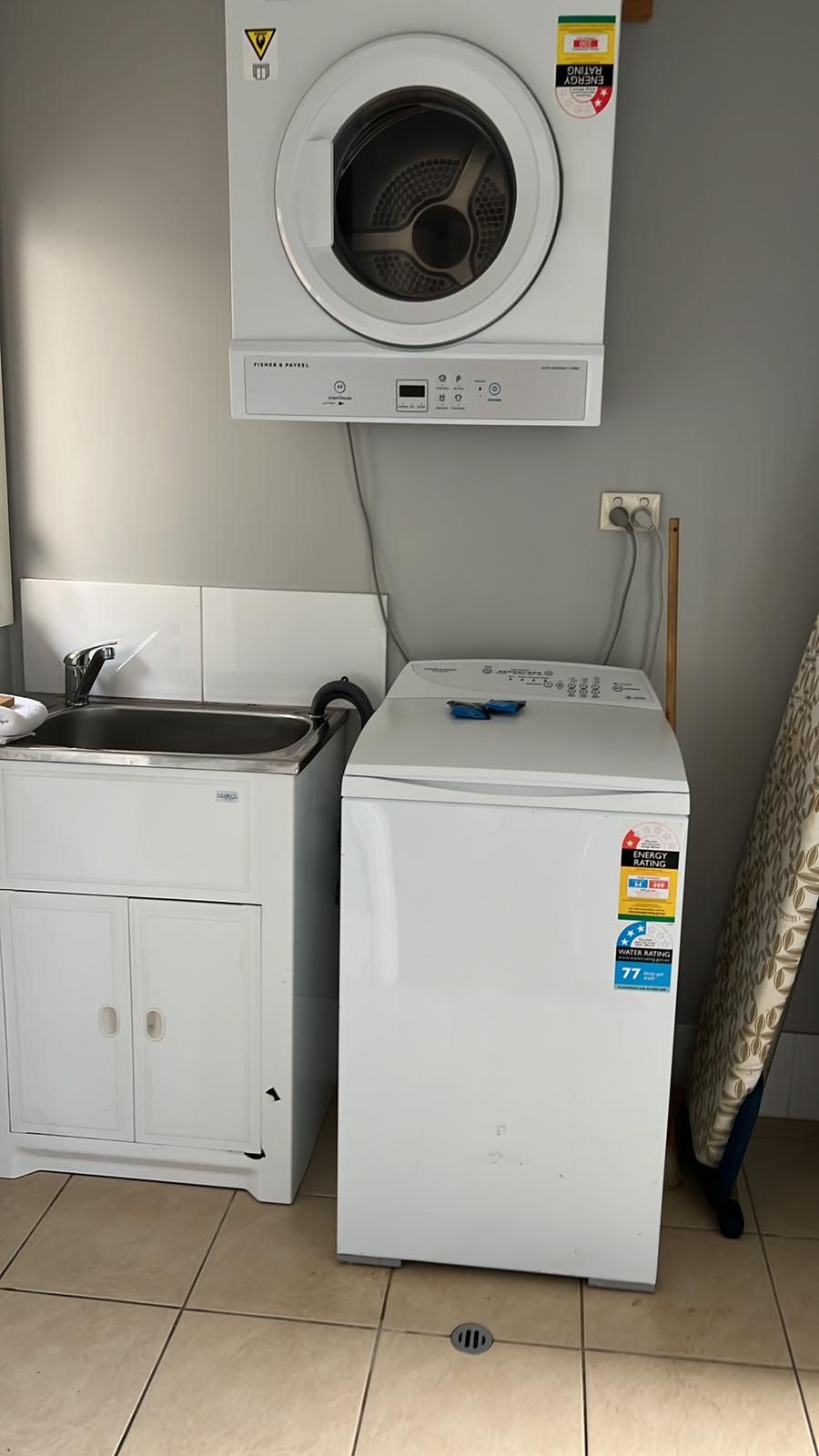 A compact laundry area with a front-loading washer and dryer, a sink, and a power outlet.