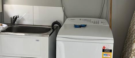 A compact laundry area with a front-loading washer and dryer, a sink, and a power outlet.