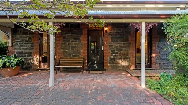 A brick building with a covered entrance, a bench, and a potted plant. - Cozy Bluestone House in Norwood – Perfect for Families and Their Pets (Norwood)