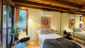 A cozy bedroom with a wooden ceiling, a large bed with a grey blanket, a bedside table with a lamp, and a potted plant. - Cozy Bluestone House in Norwood – Perfect for Families and Their Pets (Norwood)