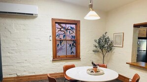 A dining area with a round table, six brown chairs, a potted plant, and a decorative window with a tree design. - Cozy Bluestone House in Norwood – Perfect for Families and Their Pets (Norwood)