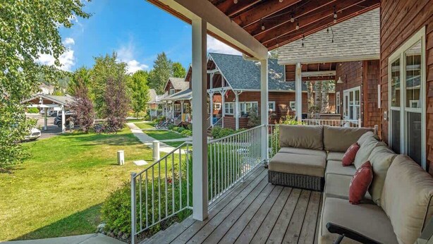 Une terrasse en bois avec un canapé et des coussins, donnant sur une pelouse bien entretenue et les maisons voisines.