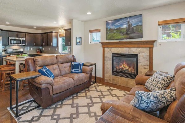 A modern living room with a fireplace, leather sofa, and a kitchen in the background. - Darling Dover Sleeps 8 - Marina, beach, trails (Dover)