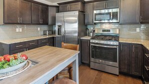Une cuisine moderne avec des meubles de couleur bois foncé, des appareils électroménagers en acier inoxydable et une table à manger en bois.