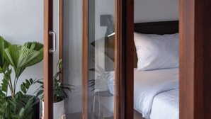Un dormitorio con un armario de madera, una cama con ropa de cama blanca y una planta en maceta.
