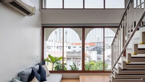 Una sala moderna con un sofá, una escalera y grandes ventanales con vista a la ciudad.