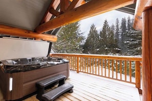 Eine Holzterrasse mit Whirlpool und Treppe, mit Blick auf eine verschneite Berglandschaft.