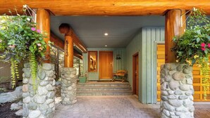 A stone pillar entrance with a wooden porch, a wooden door, and a bench. - Mountain chalet w/ hot tub & games (Whistler)