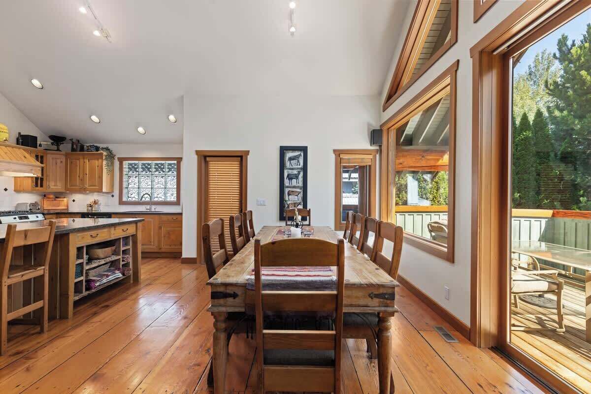 A spacious kitchen with wooden cabinets, a dining table with chairs, and large windows.