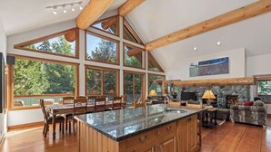 A spacious kitchen with a large island, wooden beams, and a stone fireplace. - Mountain chalet w/ hot tub & games (Whistler)
