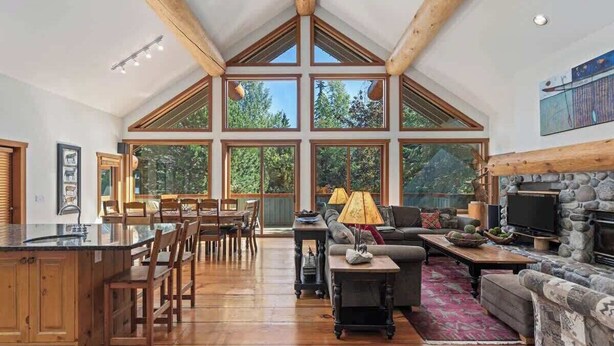A spacious living area with a large wooden ceiling, a stone fireplace, and a dining area with wooden furniture. - Mountain chalet w/ hot tub & games (Whistler)