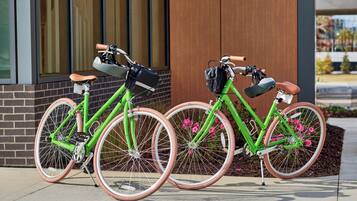 Two green bicycles with pink rims parked in front of a building with large windows and a brick facade.