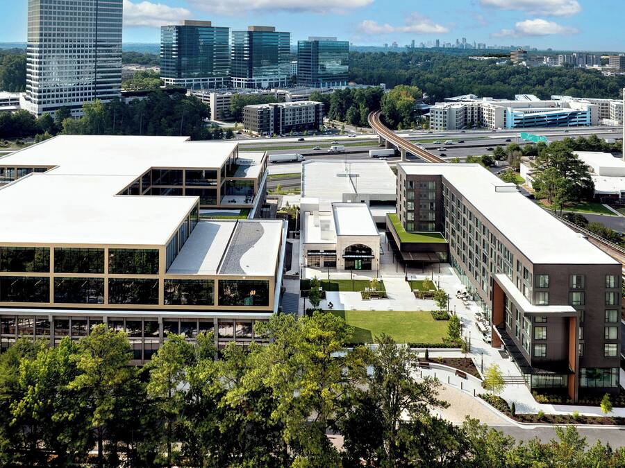 A modern building complex with multiple floors, large windows, and a green roof.