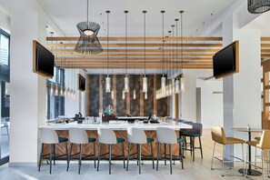 A modern bar area with a long counter, multiple bar stools, hanging pendant lights, and two flat-screen TVs mounted on the wall. - Element by Marriott Atlanta Perimeter Center (Atlanta)