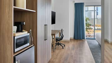A modern kitchen with a microwave, coffee maker, and refrigerator. There is a dining table with a chair and a large window with curtains.