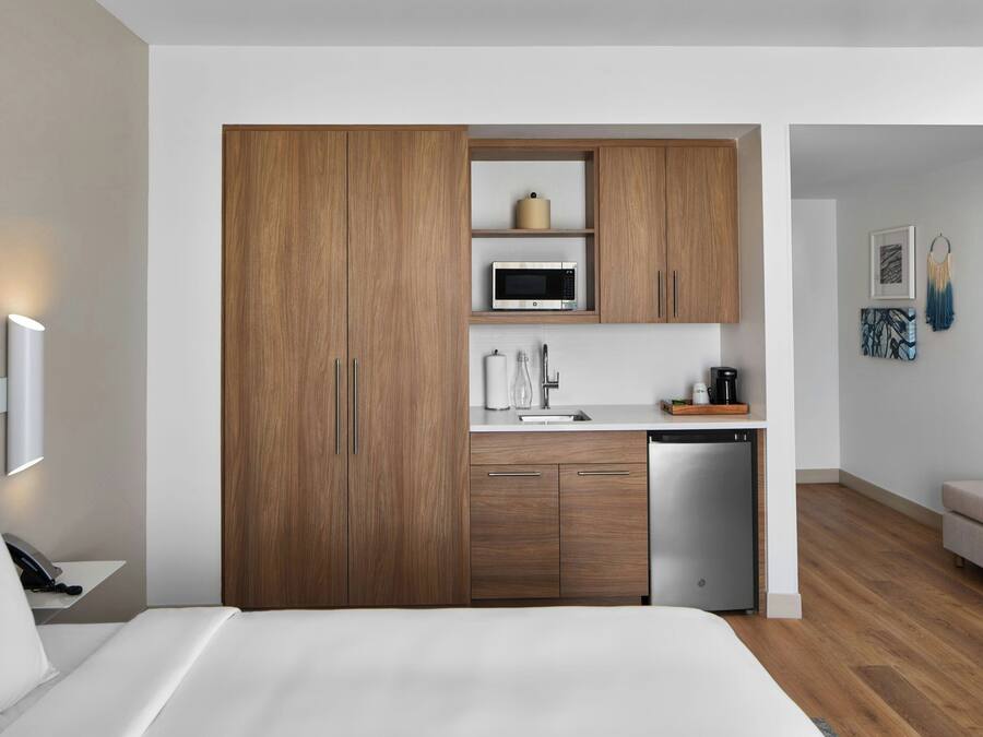Une chambre d’hôtel moderne équipée d’une armoire en bois, d’un four à micro-ondes, d’un évier et d’un lave-vaisselle compact.