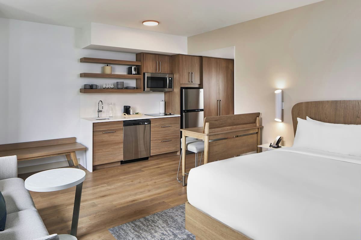 A modern hotel room with a bed, a small desk, a microwave, a refrigerator, and a sink.