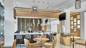 A modern restaurant with round tables and bar seating, a wooden ceiling design, and a TV mounted on the wall.