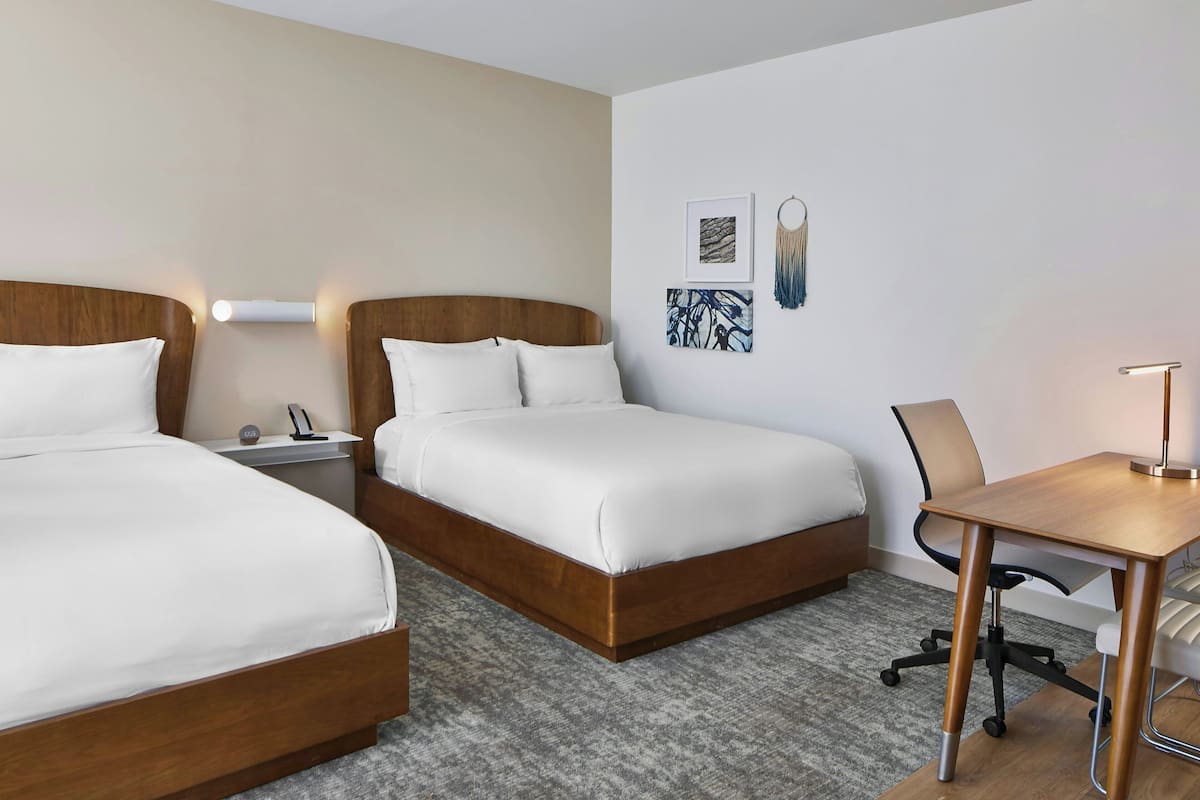 A hotel room with two beds, a desk, and a chair.