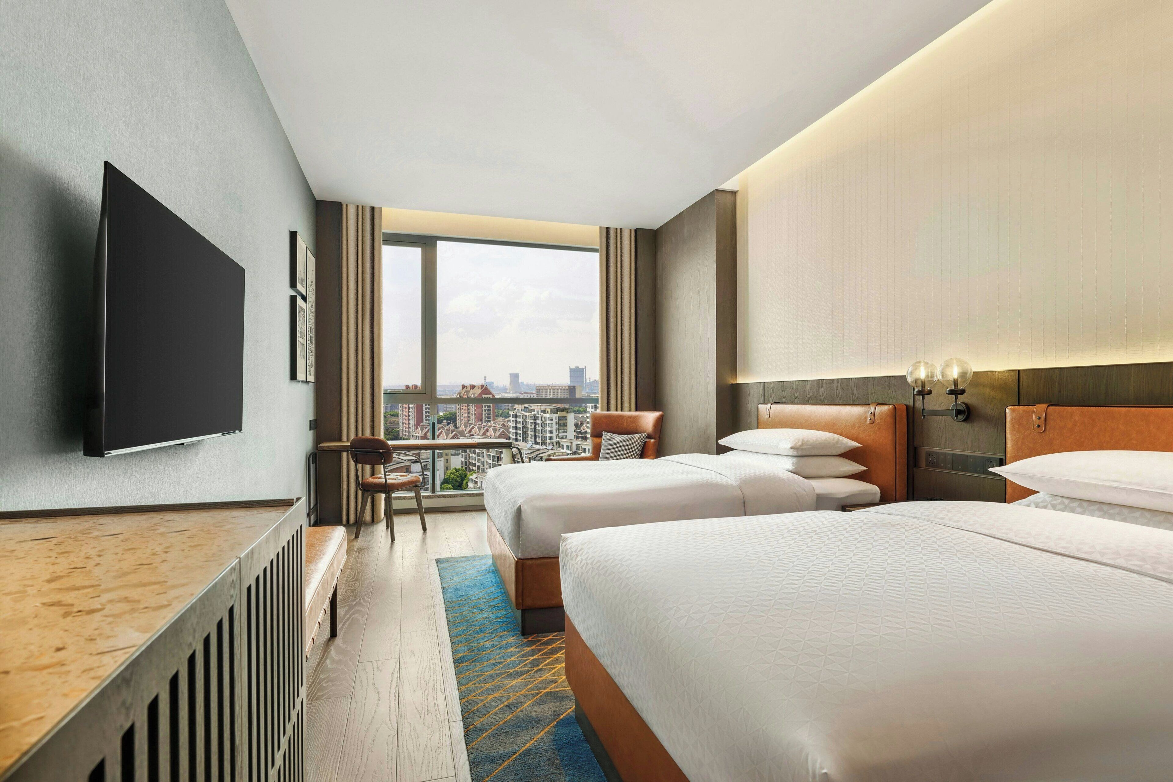 Ett hotellrum med två sängar, ett skrivbord, en TV och utsikt över staden.