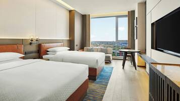 A hotel room with two beds, a sofa, a TV, and a view of the city.
