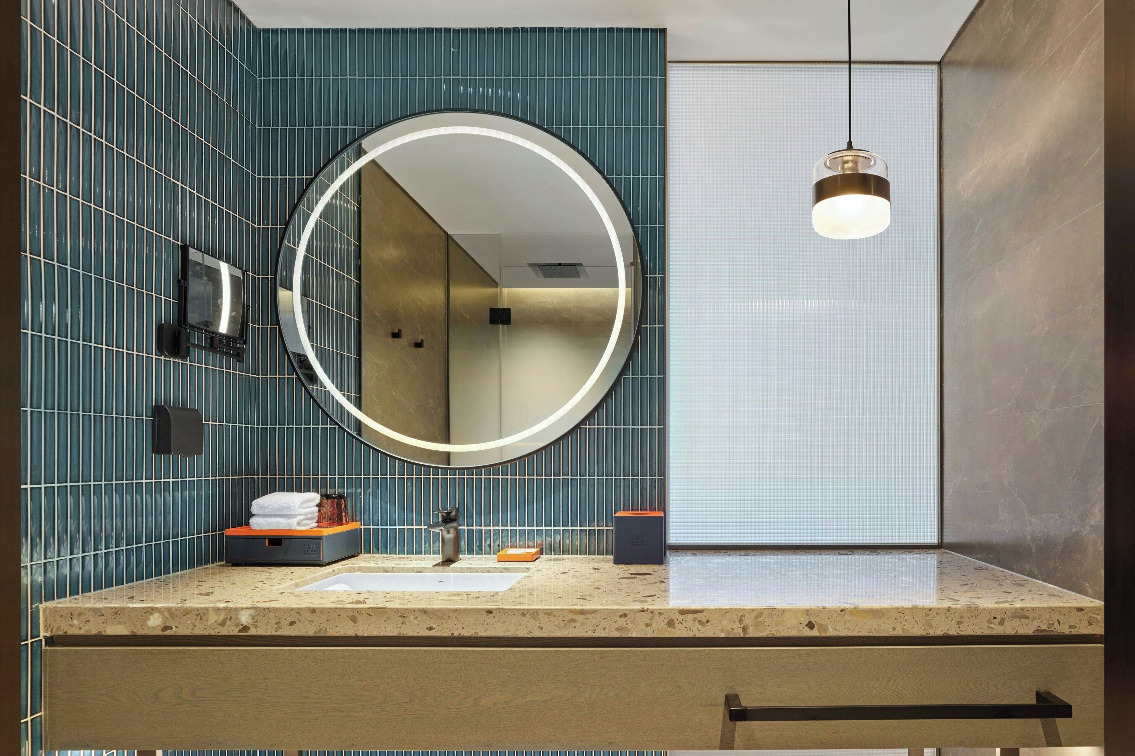Ein modernes Badezimmer mit rundem Spiegel, Waschbecken und Handtuchhalter.