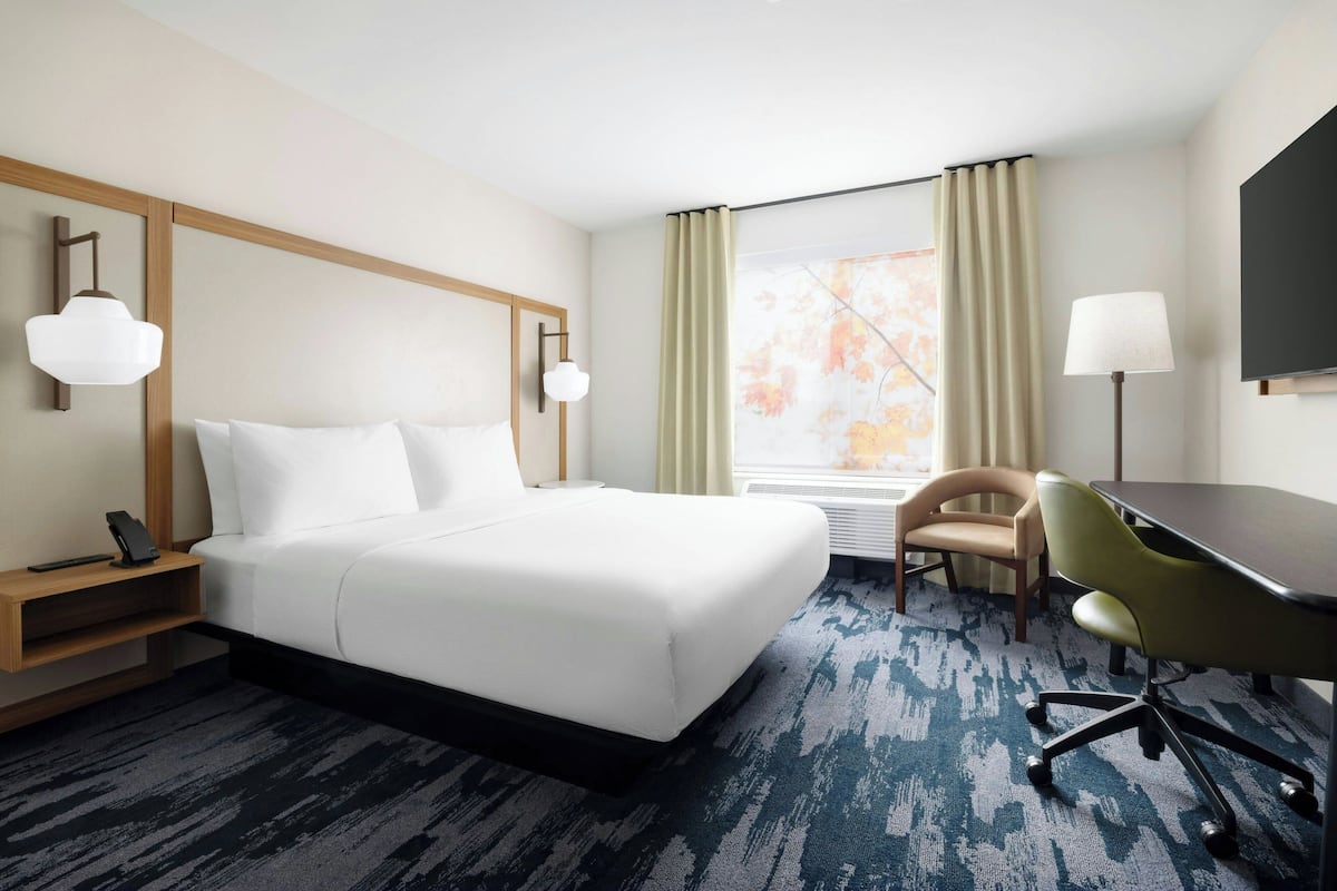 A hotel room with a large bed, a desk, a chair, a flat-screen TV, and a window with curtains.