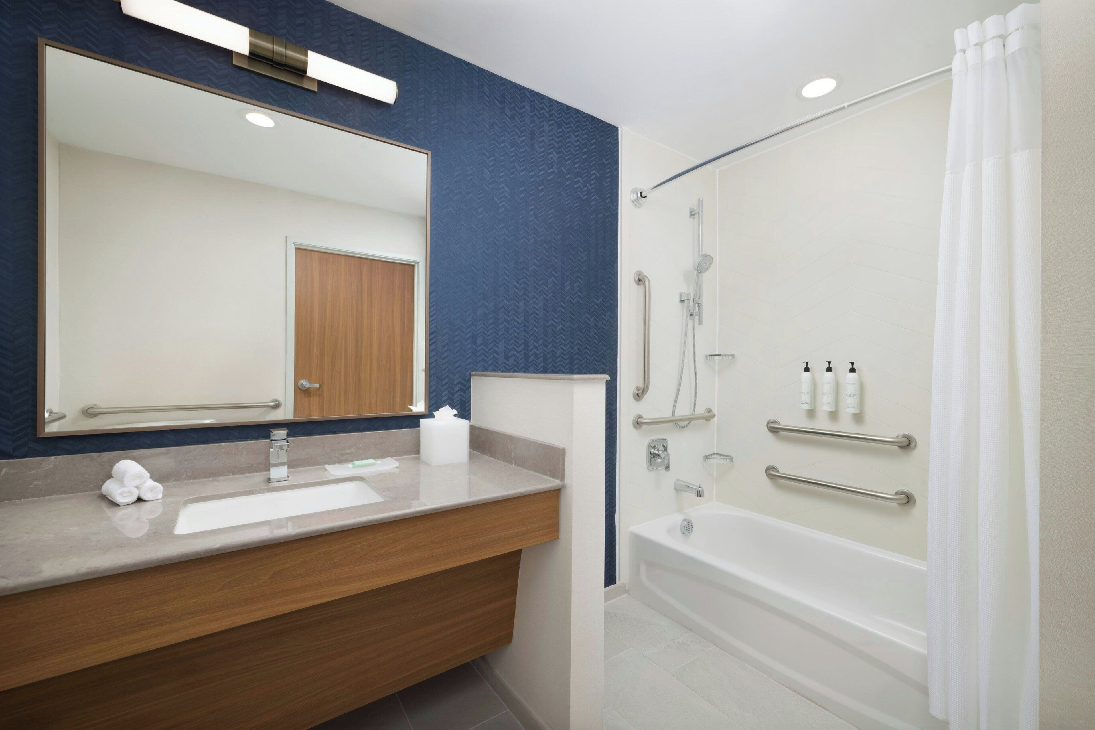 A modern bathroom with a wooden vanity, a large mirror, a bathtub, and a shower area.
