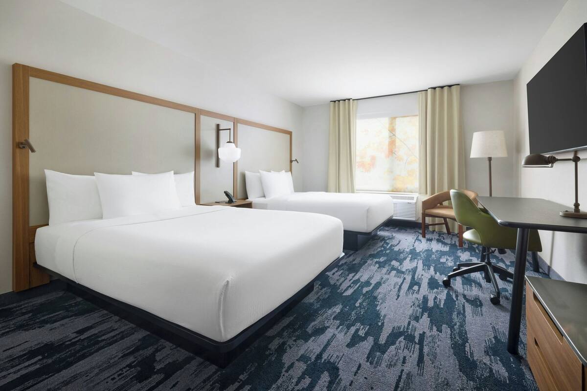 A hotel room with two beds, a desk, a chair, a TV, and a window with curtains.